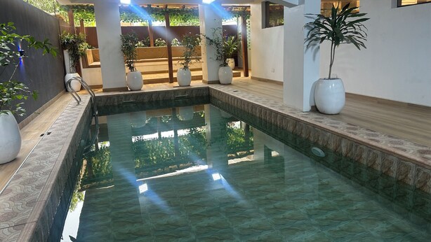 An indoor swimming pool with clear water, surrounded by white pillars and potted plants.