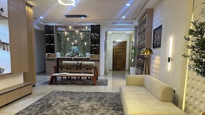 A modern living room with a sofa, a patterned rug, a dining area with a table and chairs, and a decorative wall with a plant.