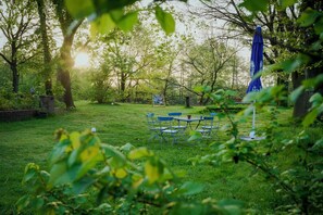 A grassy outdoor area with a table and chairs, surrounded by trees and a blue umbrella. - House by the lake with plenty of space, right next to the Lüneburg Heath parks (Rethem)
