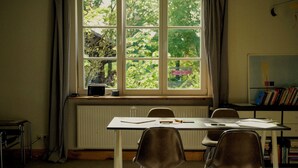 A room with a large window, a radiator, a table with chairs, and a bookshelf. - House by the lake with plenty of space, right next to the Lüneburg Heath parks (Rethem)