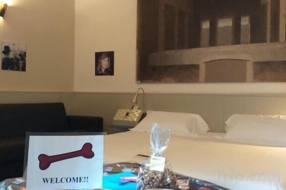 A hotel room with a bed, a bedside table with a welcome sign, a nightstand, and a wall-mounted phone.