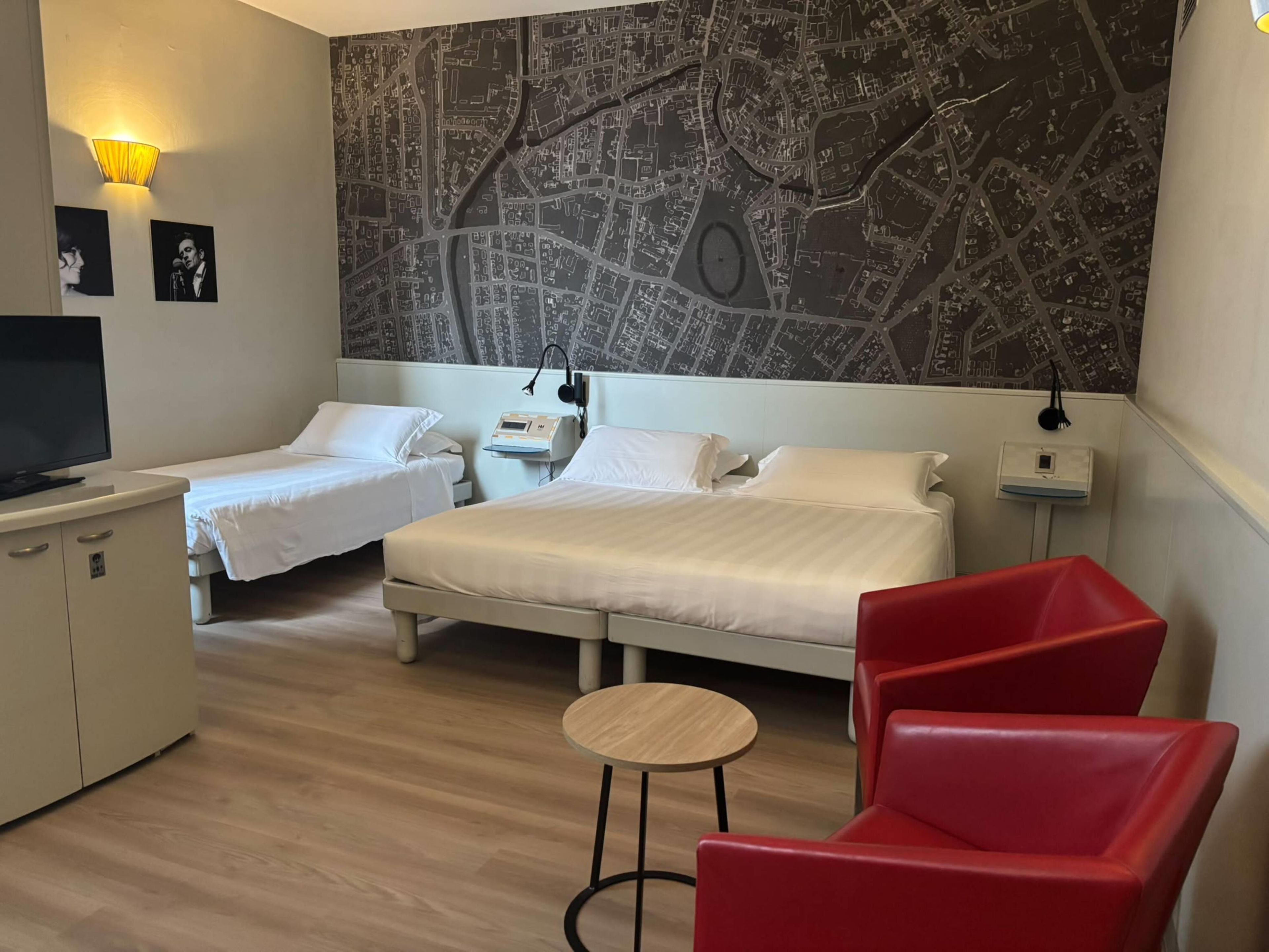 A hotel room with two beds, a TV, a map on the wall, and a red chair.