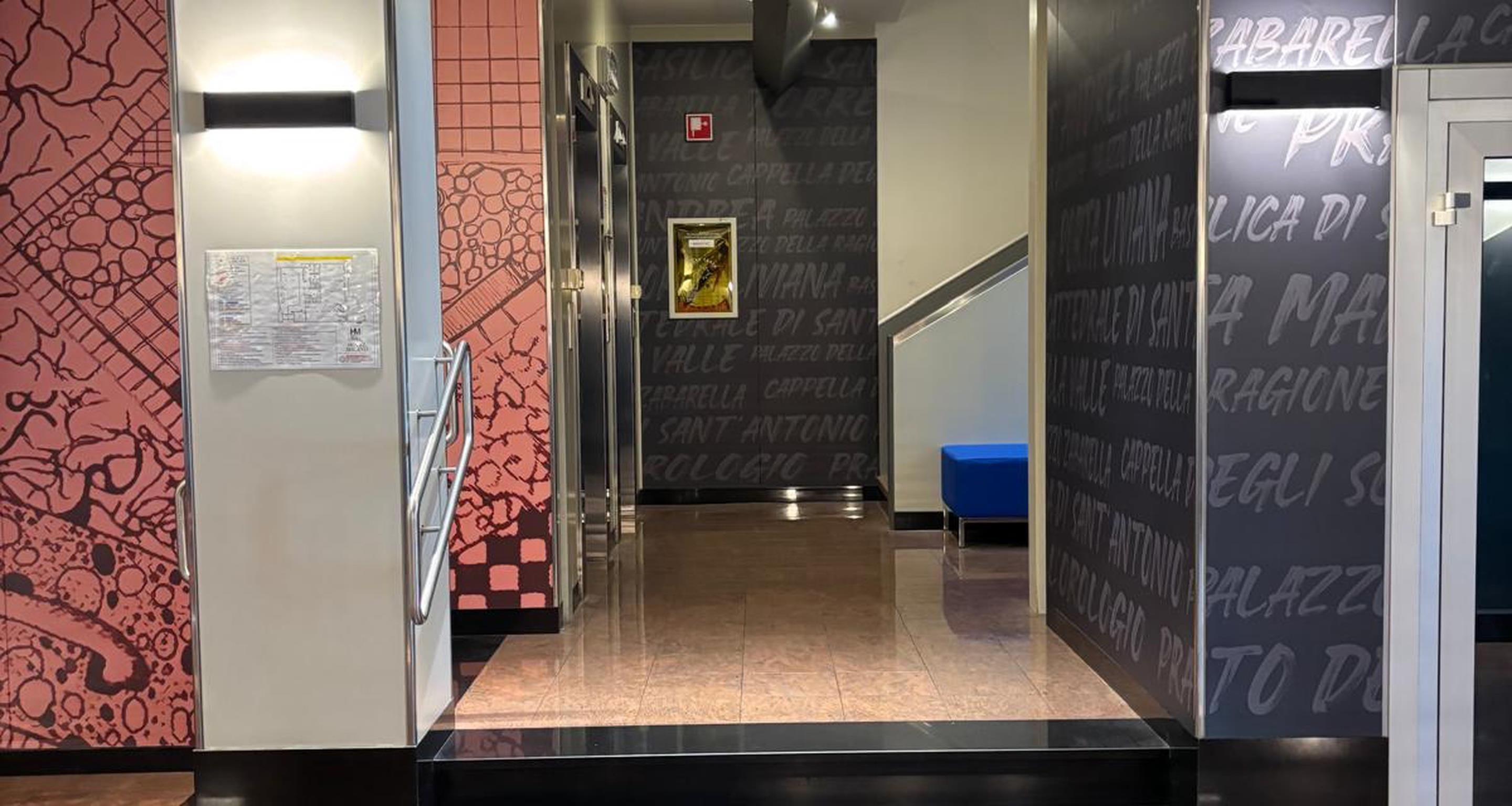 A hallway with a patterned wall, a blue trash bin, and a door with a sign.