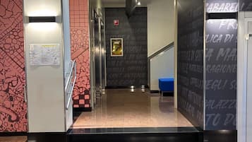 A hallway with a patterned wall, a blue trash bin, and a door with a sign.