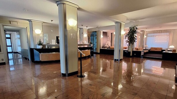 A spacious lobby with a polished marble floor, a reception desk, and a statue of a figure.