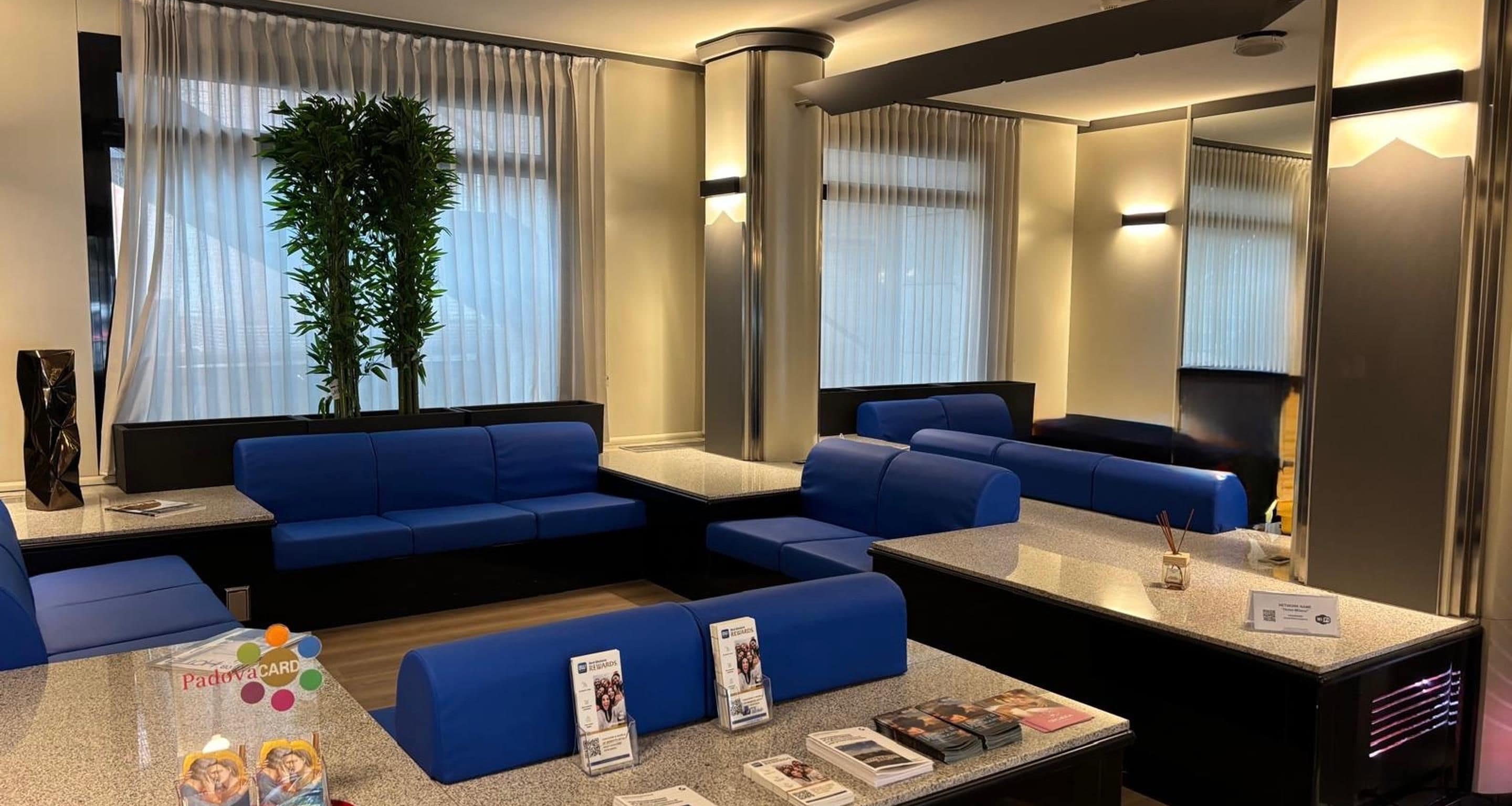 Un vestíbulo de hotel con asientos azules, un mostrador de recepción y un espejo grande.