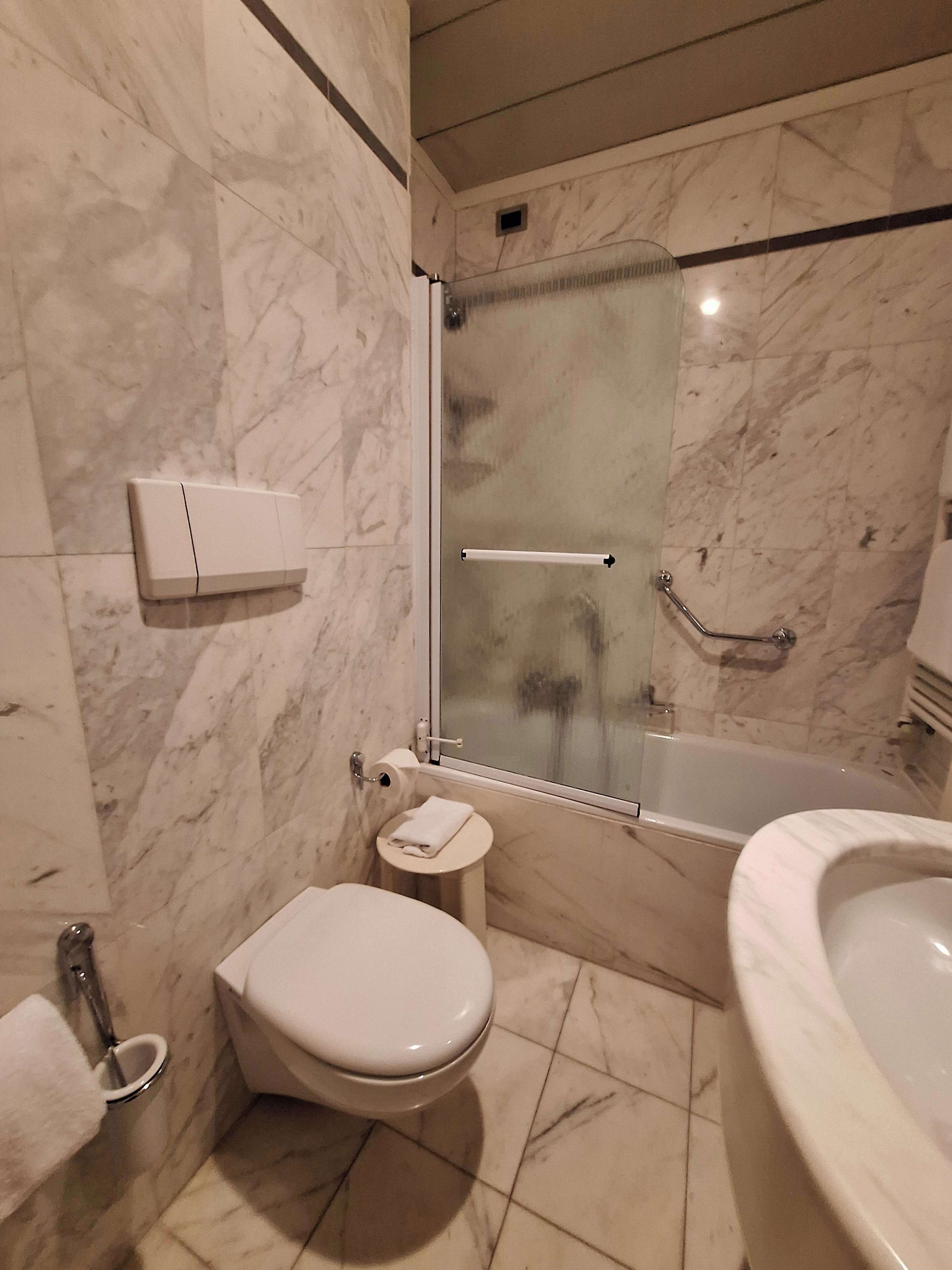 Une salle de bain moderne comprenant des toilettes, une petite table de chevet, une douche à parois de verre et une baignoire.