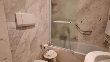 Een moderne badkamer met toilet, een klein nachtkastje, een douche met glazen wanden en een bad.