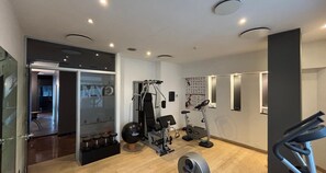Un gimnasio moderno con diversos equipos de ejercicio, incluyendo una cinta de correr, máquinas de pesas y un espejo adosado a la pared.