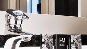 A modern bathroom with a chrome faucet, a black vertical sign with 'HM HOTEL MILANO PADOVA' text, and a mirror reflecting the room. - Sure Hotel By Best Western Milano (Padova)