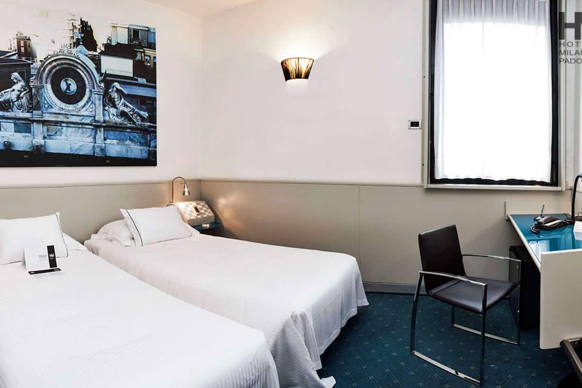 Une chambre d’hôtel avec deux lits, un bureau, une chaise, une lampe, une horloge et une fenêtre.