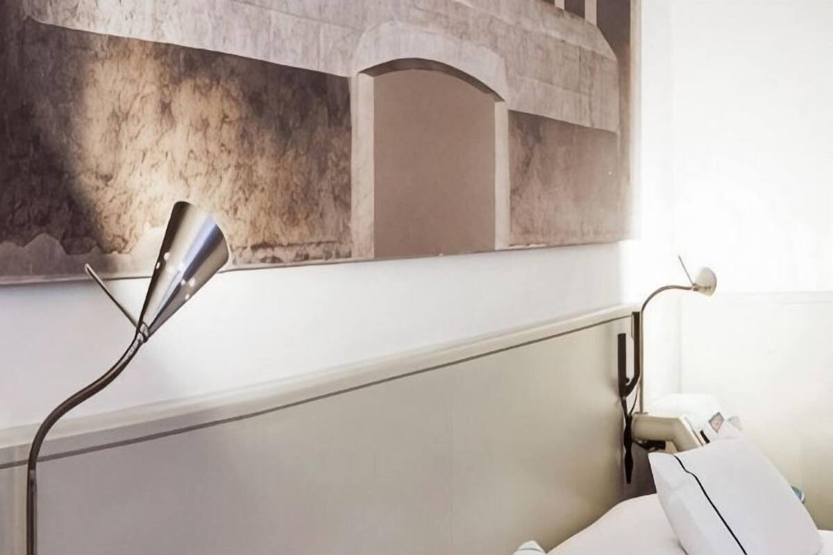 Una habitación con una cama, dos lámparas de noche, un almohadón blanco y una pared con textura.