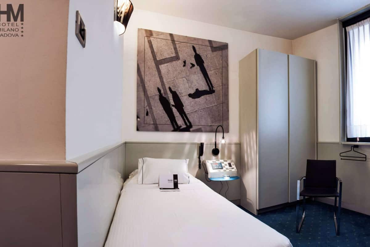Habitación de hotel con cama, escritorio con lámpara, silla, armario y ventana con cortinas.