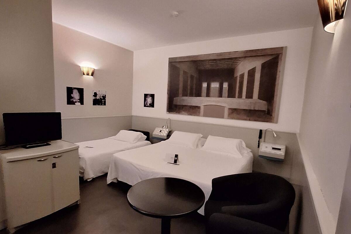 Une chambre d’hôtel avec deux lits, une télévision, une petite table et un grand tableau au mur.