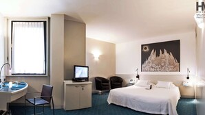 A hotel room with a bed, desk, chair, computer, and a large wall painting.