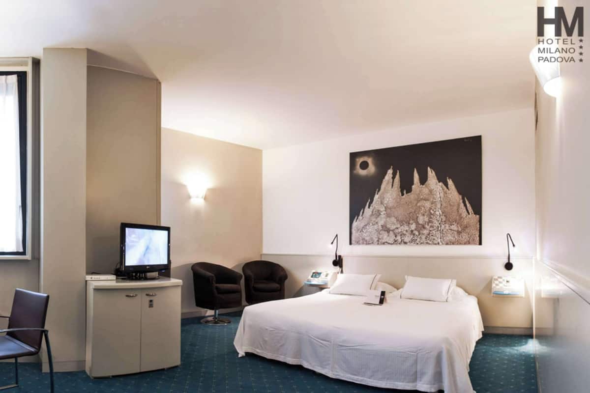 Une chambre d’hôtel équipée d’un lit, d’un bureau, d’une chaise, d’un ordinateur et ornée d’un grand tableau mural.