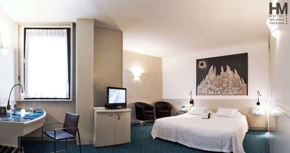 Habitación de hotel con cama, escritorio, silla, ordenador y un cuadro grande en la pared.