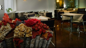 A dining area with tables and chairs, a decorative centerpiece with flowers, and wall-mounted lighting.