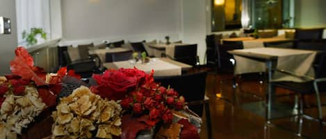 A dining area with tables and chairs, a decorative centerpiece with flowers, and wall-mounted lighting.