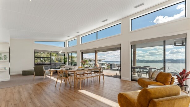 Uma sala de estar ampla com piso de madeira, uma mesa de jantar e um sofá. Grandes janelas oferecem vista para o exterior.