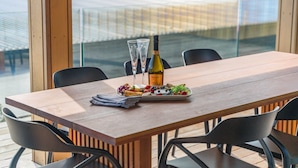 Uma mesa de jantar com uma garrafa de vinho, dois copos e um prato de frutas em um terraço com cadeiras.