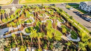An aerial view of a landscaped area with winding paths, palm trees, and a parking lot with cars. - Themed Bedrooms, Game Room & Private Pool with BBQ – Minutes from Disney (Clermont)