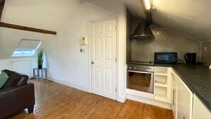 A compact kitchen with a built-in oven and microwave, a white door, and a small side table with a plant. - City Centre 2bed Apartment Wi-fi Parking (Newcastle-upon-Tyne)