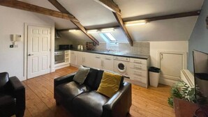 A loft-style apartment with exposed wooden beams, a kitchenette, a washing machine, and a leather sofa. - City Centre 2bed Apartment Wi-fi Parking (Newcastle-upon-Tyne)