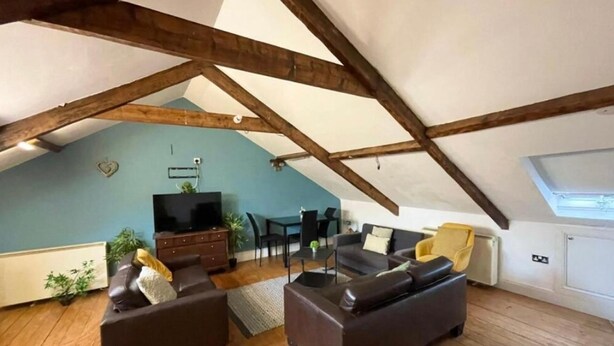A loft-style living room with exposed wooden beams, a flat-screen TV, dark sofas, and a dining table with chairs. - City Centre 2bed Apartment Wi-fi Parking (Newcastle-upon-Tyne)