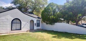 Uma casa térrea com fachada branca, porta de entrada e pequeno jardim frontal.