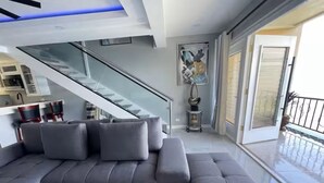 A modern living room with a grey sectional sofa, a staircase, and a balcony with a railing.