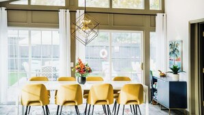 Un comedor con mesa y sillas, una lámpara colgante y vistas amplias a través de ventanas grandes.