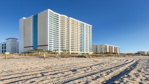 Et strandhotel med flere høje bygninger, en sandstrand og en klar blå himmel.
