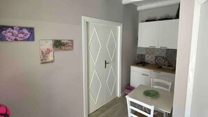 Una cocina compacta con armarios blancos, una mesa de comedor y una puerta con diseños de rombos.
