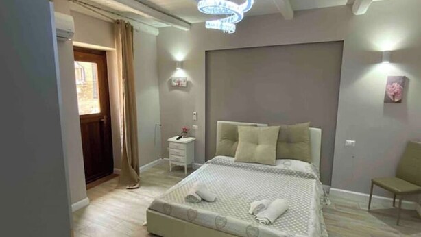 Un dormitorio moderno con una cama grande, mesitas de noche, un pequeño escritorio y una silla, con una araña de cristal.