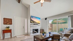 A living room with a fireplace, a ceiling fan, a television, and a sliding glass door to a patio. - Perfect Chandler Getaway – Cozy Condo in the Heart of the East Valley! (Chandler)