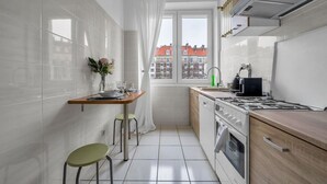 A compact kitchen with white tiles, a wooden countertop, a gas stove, a dishwasher, and a window with a view of buildings.