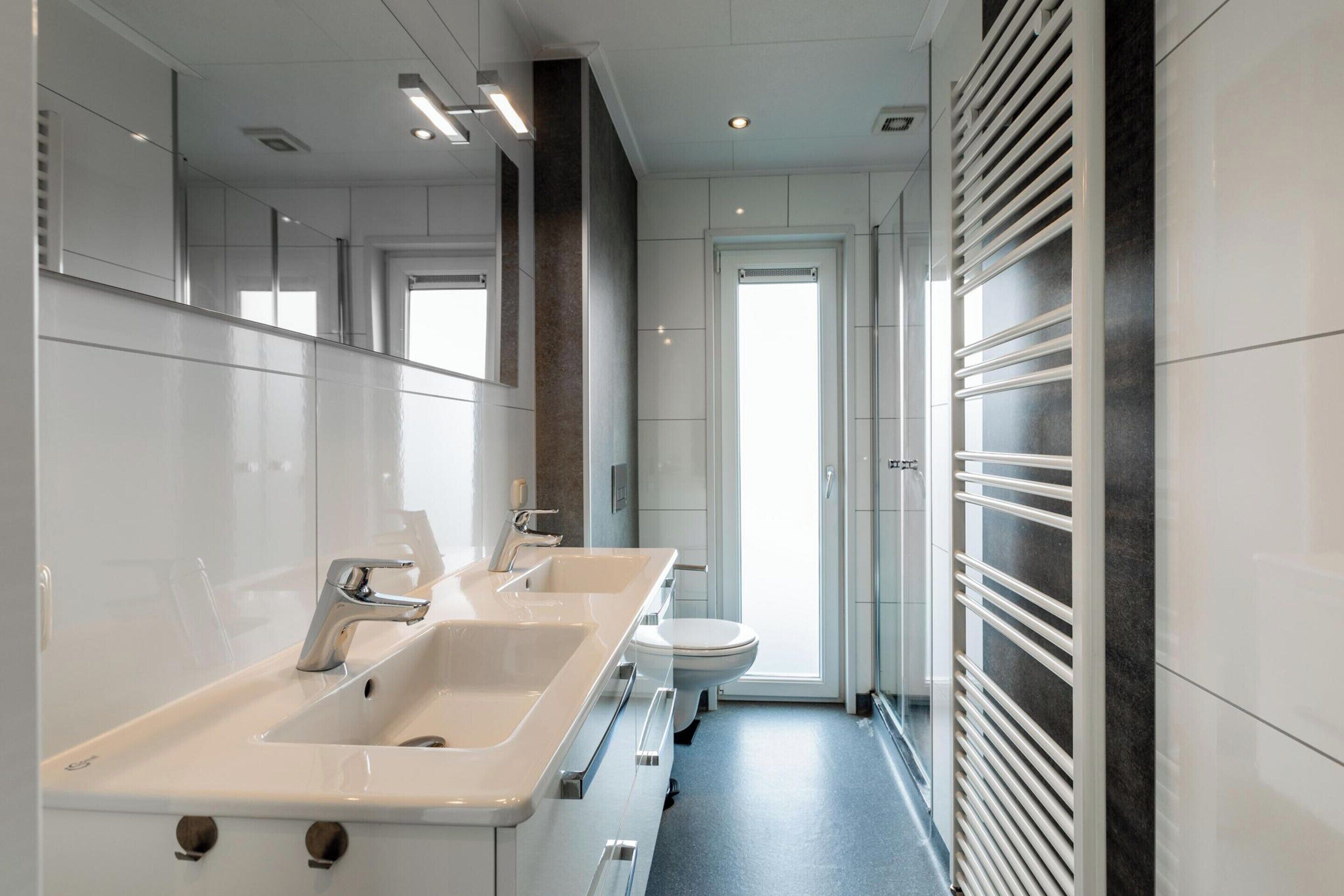 A modern bathroom with dual sinks, a toilet, and a glass shower enclosure.