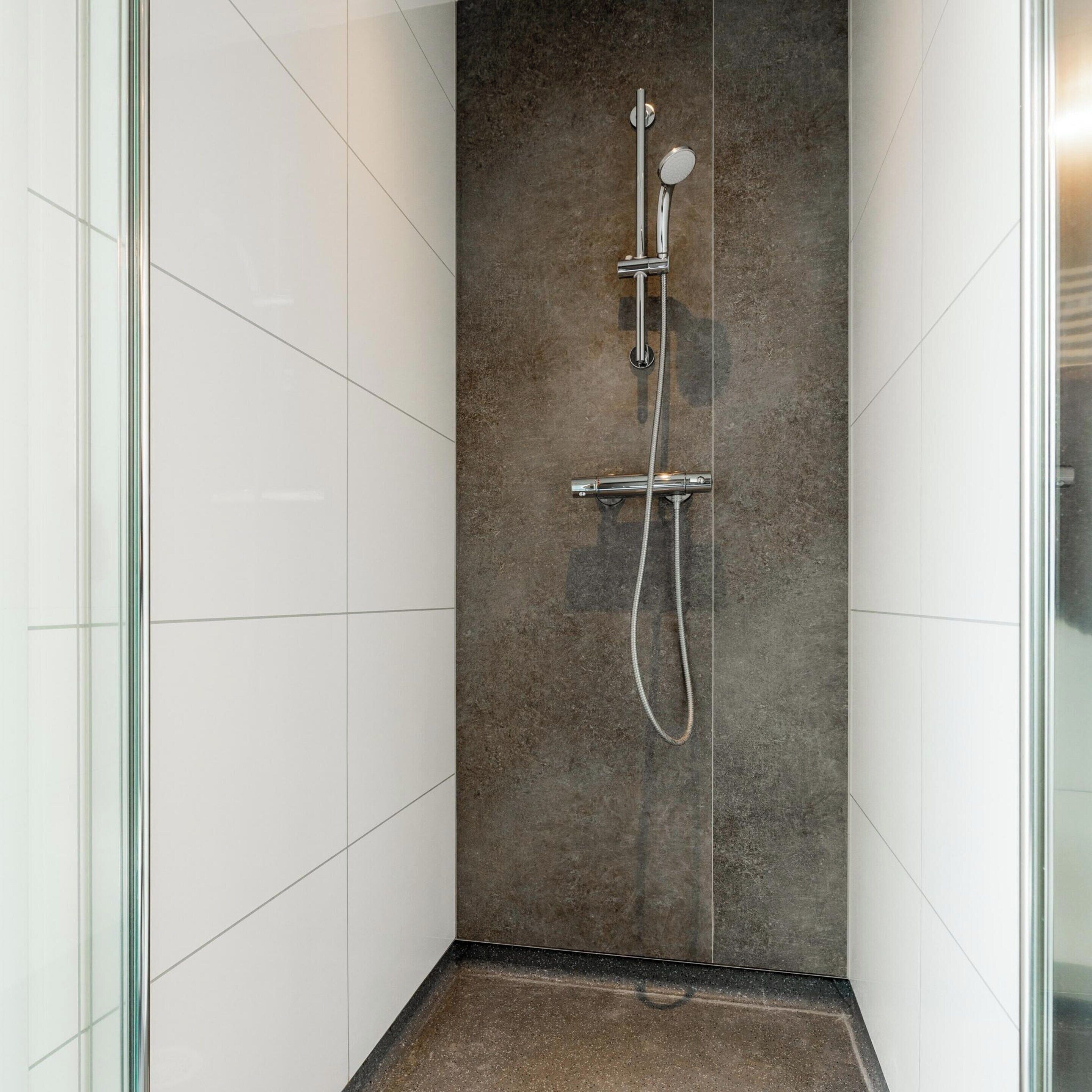 Une douche moderne dotée d’une paroi en verre, d’un mur recouvert de carreaux foncés et d’un pommeau de douche chromé.