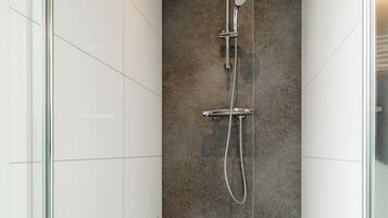 Une douche moderne dotée d’une paroi en verre, d’un mur recouvert de carreaux foncés et d’un pommeau de douche chromé.