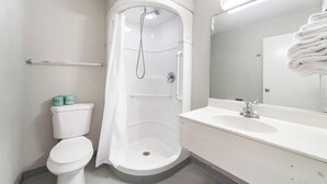 A bathroom with a white toilet, a shower with a glass door, a sink with a mirror, and a towel rack. - Extended Stay by Welcome INN (Blue Springs)