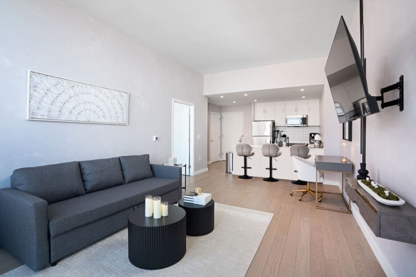 Una sala de estar moderna con un sofá gris, una mesa de centro con velas y una cocina al fondo.