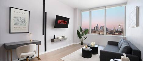 Un salon moderne avec un bureau, un canapé, un téléviseur et une vue sur la ville.