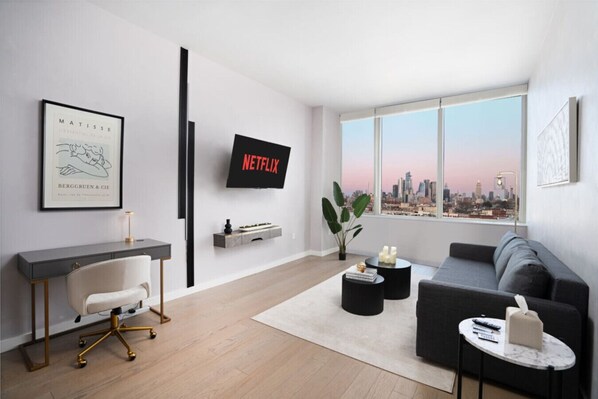 Una sala de estar moderna con un escritorio, un sofá, un televisor y vistas a la ciudad.