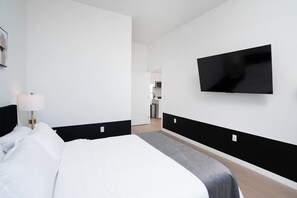 Habitación de hotel con cama, televisor de pantalla plana en la pared y una kitchenette al fondo.