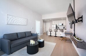 Een moderne woonkamer met een grijze bank, een zwarte salontafel en een aan de muur bevestigde televisie.