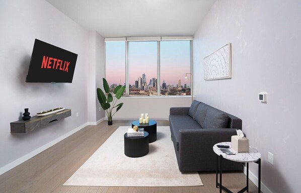Een moderne woonkamer met een groot raam, een flatscreen-televisie, een grijze bank, een salontafel en een bijzettafeltje.