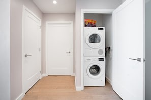 Un lavadero con lavadora y secadora apiladas, una puerta y piso de madera.