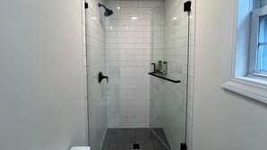 A narrow shower area with white tiled walls, a black showerhead, and a shelf with toiletries.