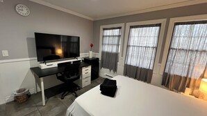 A bedroom with a bed, a desk with a TV, a chair, and a window with curtains.